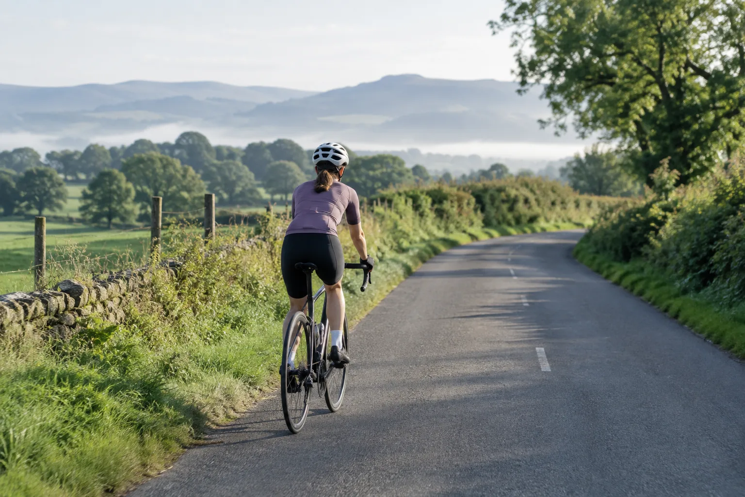 Un cycliste débutant roule sur une route calme bordée de campagne.